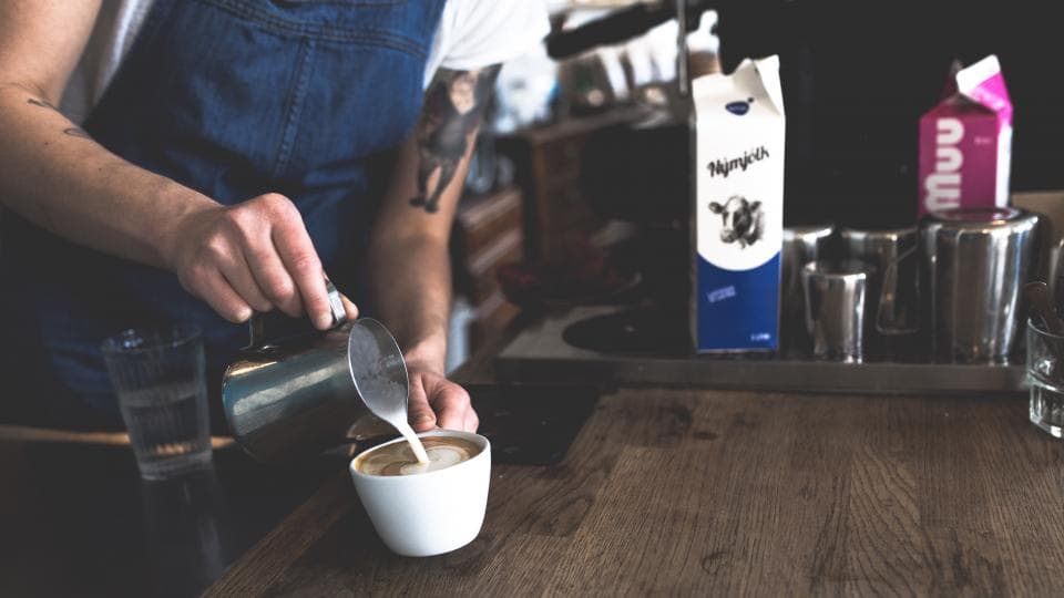 A barista pouring milk into a coffee